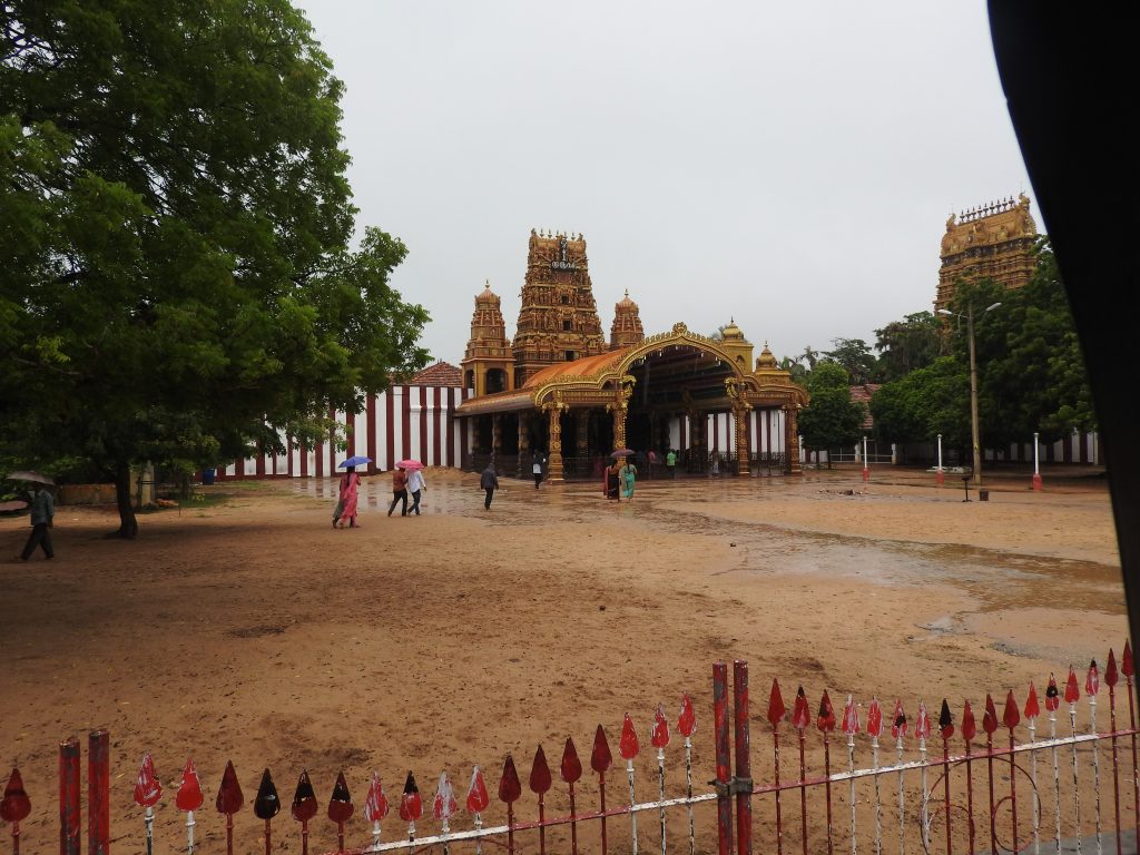 The golden arched entrance and carved gateway tower of Nallur Kandaswamy Temple behind a wide sandy forecourt, with red-and-white striped walls
