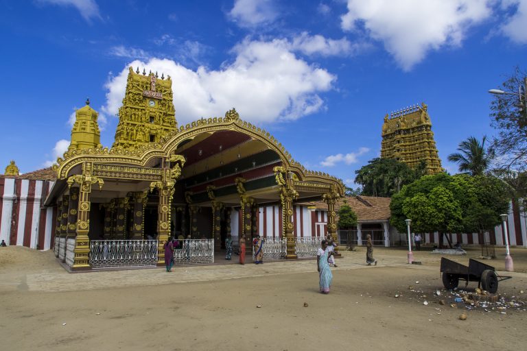 The golden arched entrance pavilion of Nallur Kandaswamy Temple, with a carved gateway tower behind it and a second tower to the right, under a blue sky