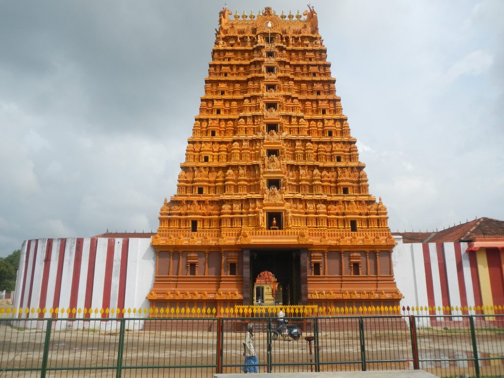 A tall, ornately carved orange gateway tower at Nallur Kandaswamy Temple, set in red-and-white striped walls