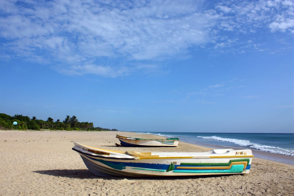 Two fishing boats pulled up on the wide sand of Nilaveli beach, with small waves breaking on the shore