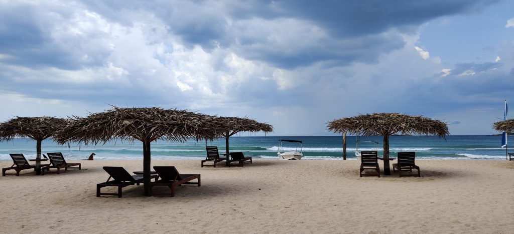 Thatched sun shades and loungers on the sand at Nilaveli beach near Trincomalee, with a calm sea and grey clouds breaking up overhead