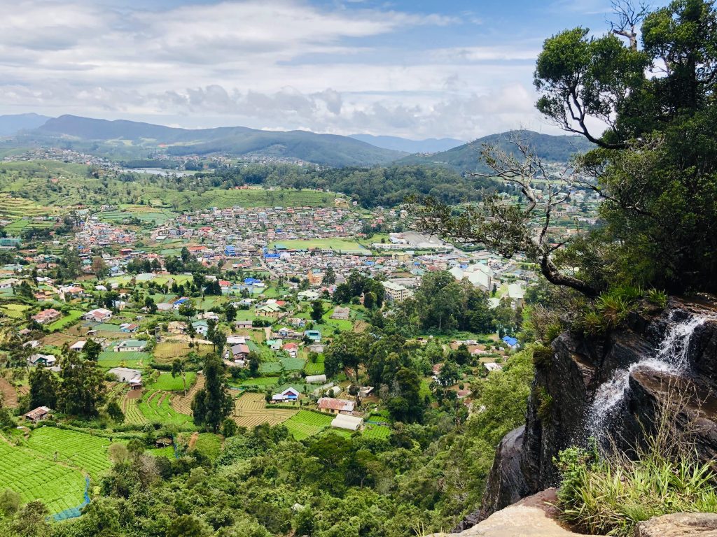 View from the rocks beside Lover's Leap over the roofs of Nuwara Eliya and surrounding tea and vegetable terraces, with a small cascade on the right