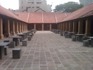A paved courtyard at the Old Dutch Hospital in Colombo, with low tile-roofed verandas on either side and stone tables and stools