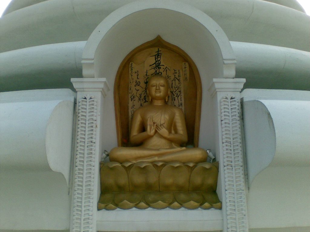 A gilded seated Buddha in an arched niche of the white pagoda, with Japanese calligraphy on the wall behind