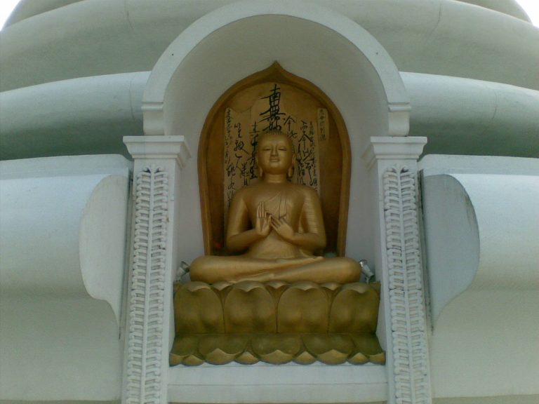 A gilded seated Buddha in an arched niche of the white pagoda, with Japanese calligraphy on the wall behind