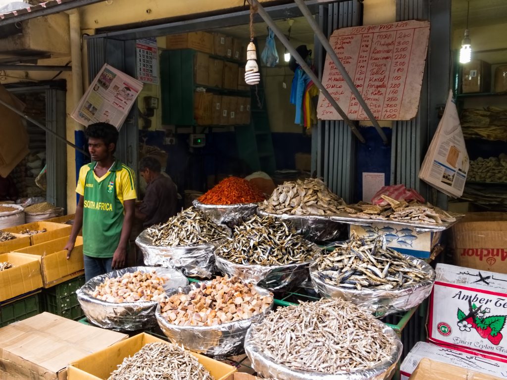 A dried-fish shop in Pettah, Colombo, with foil-lined baskets of small dried fish and chillies in front of a hand-written price list