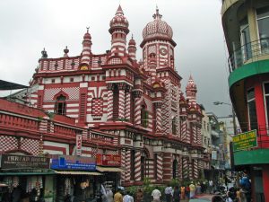 The red-and-white striped Jami Ul-Alfar Mosque with its domes and clock tower, above shops on a Pettah street