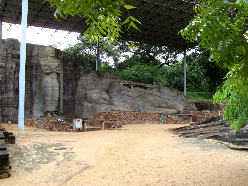 Standing Buddha and long reclining Buddha carved into the same rock face at Gal Vihara, under a metal roof