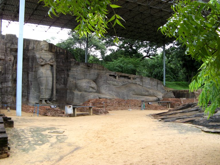 Standing Buddha and long reclining Buddha carved into the same rock face at Gal Vihara, under a metal roof