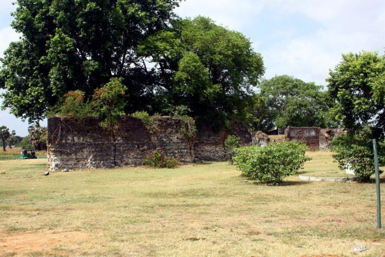 Brick and stone wall remains of Pooneryn Fort, overgrown with trees, with open grass in front