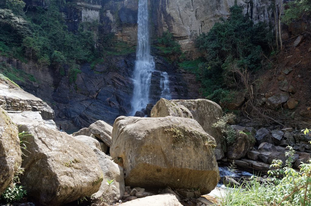 Ramboda Falls dropping down a rock face behind large boulders in the stream bed