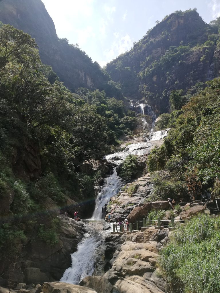 Ravana Falls cascading over rock tiers between steep forested cliffs, with the viewing railing below