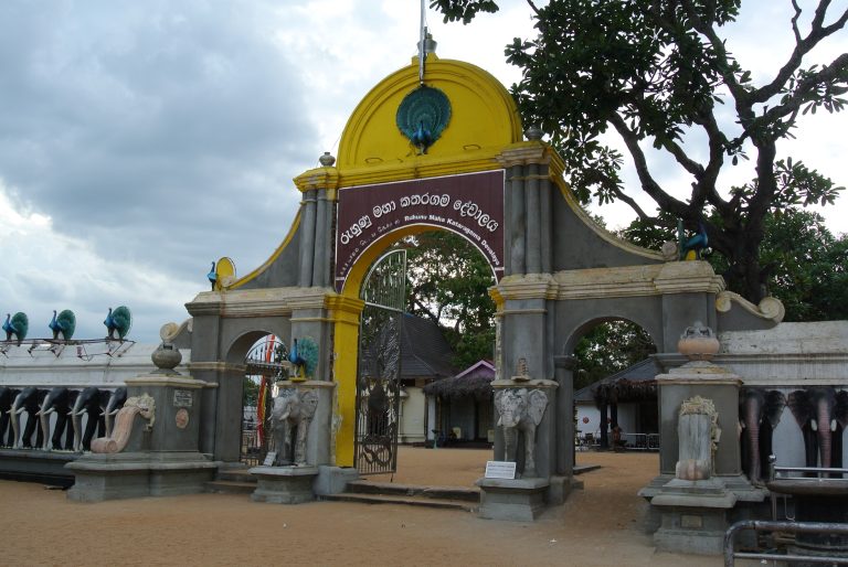 Arched gateway of the Ruhunu Maha Kataragama Devalaya, with a peacock on top, elephant statues on the pillars and a row of carved elephants along the wall
