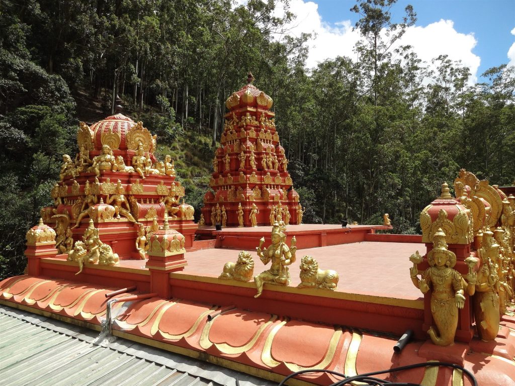 Red and gold gopuram towers and roof sculptures of Seetha Amman Temple against forested hills