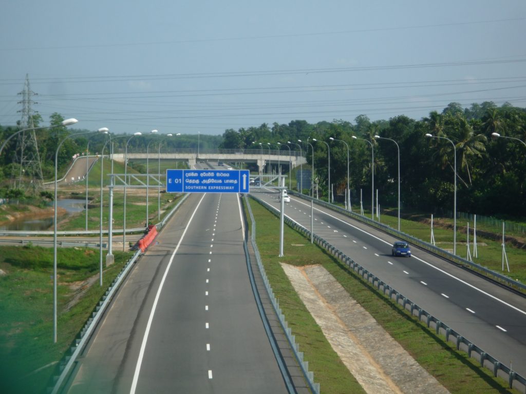 A bus on the Southern Expressway, a four-lane motorway curving towards green wooded hills under a grey sky