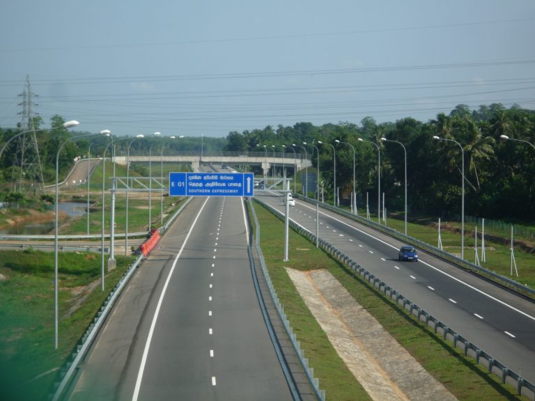 A bus on the Southern Expressway, a four-lane motorway curving towards green wooded hills under a grey sky
