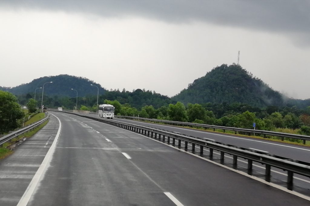 The Southern Expressway running straight between green verges and street lights, with a blue overhead sign and palm trees beside the road
