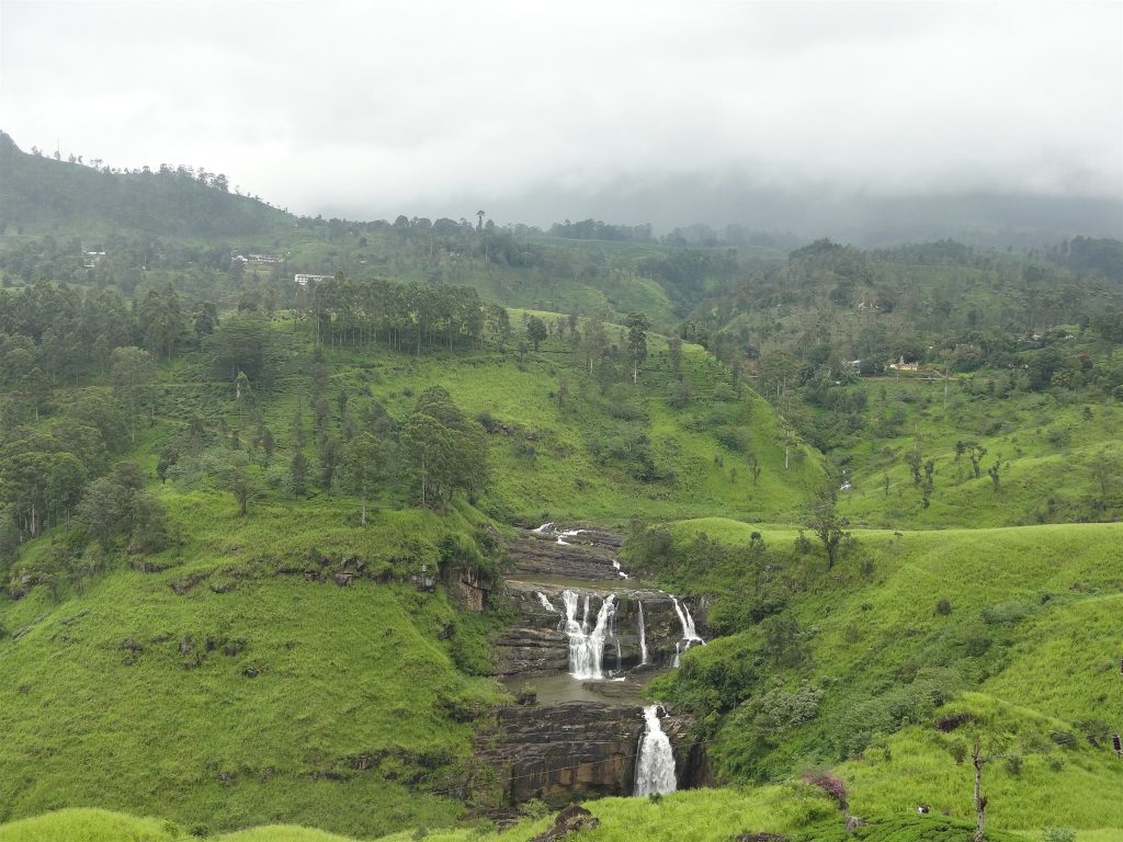 St Clair's Falls with several white cascades over dark rock ledges between steep green slopes under low cloud