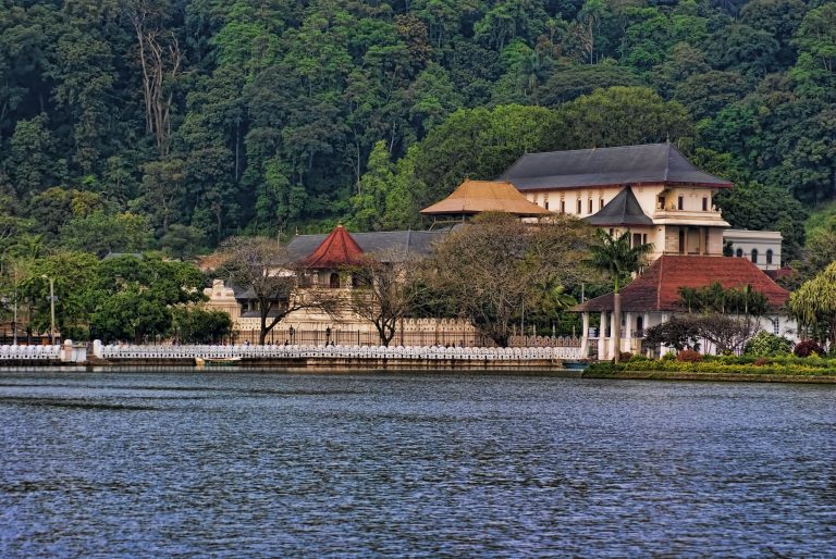 The Temple of the Sacred Tooth Relic and its octagonal tower across Kandy Lake, with forested hills behind