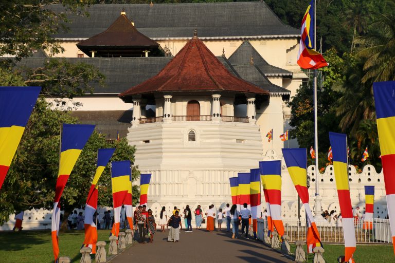 The octagonal Paththirippuwa of the Temple of the Tooth at the end of a path lined with Buddhist flags