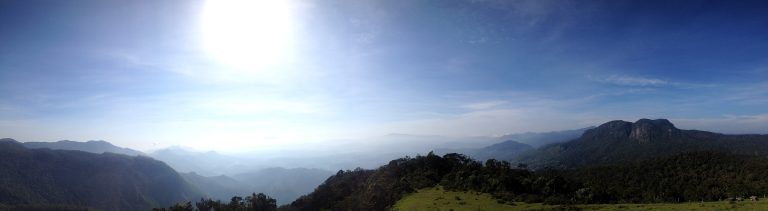 Wide panorama from the top of Moon Plains, with hazy ridges and a grassy slope under a blue sky
