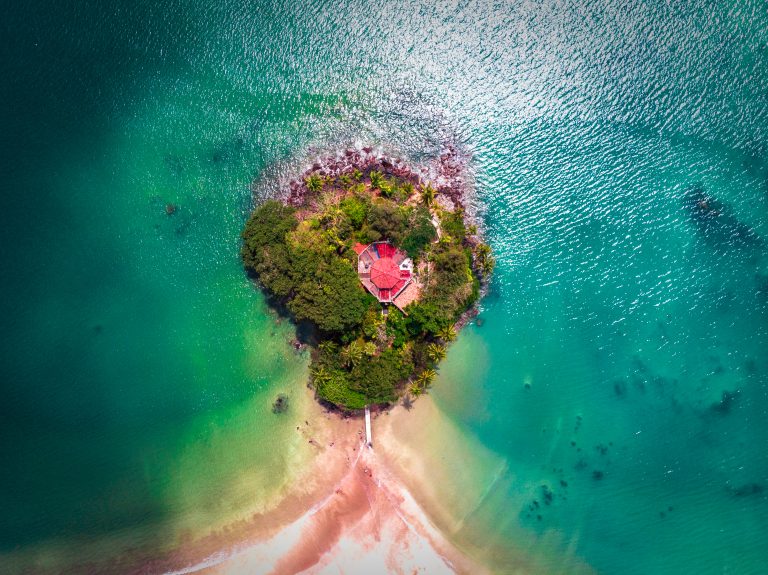Aerial view of Taprobane Island, a small wooded islet with an octagonal red-roofed villa, almost joined to the beach by a strip of sand